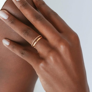 May include: A gold ring with a twisted band on a finger.