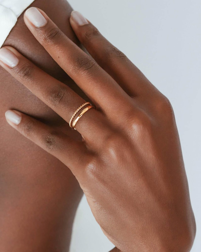 May include: A gold ring with a twisted band on a finger.