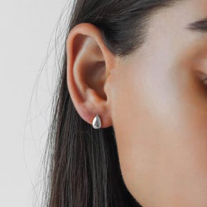 Puede incluir: Primer plano de una oreja con un pequeño pendiente de plata en forma de lágrima.