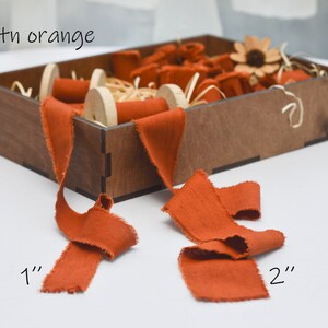 May include: A wooden box filled with spools of burnt orange ribbon. The ribbon is available in two widths: 1 inch and 2 inches.