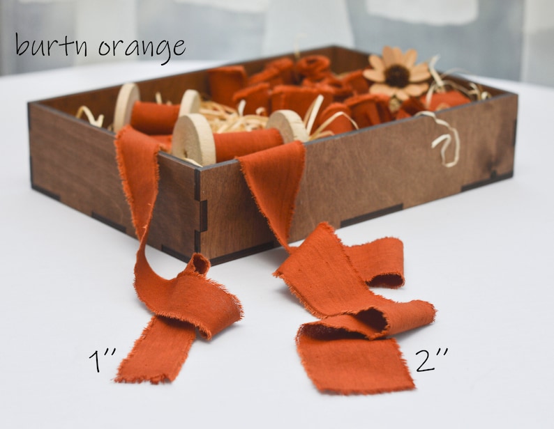 May include: A wooden box filled with spools of burnt orange ribbon. The ribbon is available in two widths: 1 inch and 2 inches.