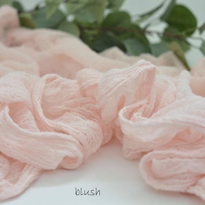 May include: A blush pink fabric ribbon, made of a soft, gauzy material, is arranged in a loose, flowing pile. The fabric has a delicate, slightly textured appearance.