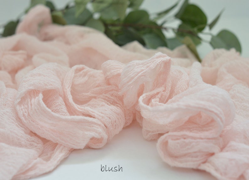 May include: A blush pink fabric ribbon, made of a soft, gauzy material, is arranged in a loose, flowing pile. The fabric has a delicate, slightly textured appearance.