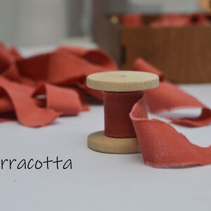 May include: A spool of terracotta colored ribbon with a wooden spool. The ribbon is frayed and has a rustic look.