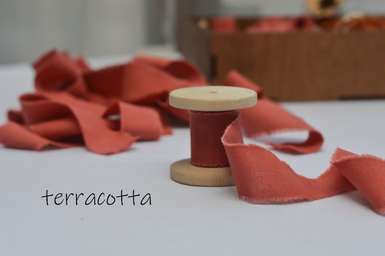 May include: A spool of terracotta colored ribbon with a wooden spool. The ribbon is frayed and has a rustic look.