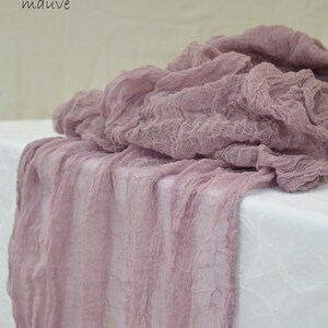May include: Mauve colored, textured, sheer fabric table runner. The fabric is loosely woven and has a crinkled appearance.