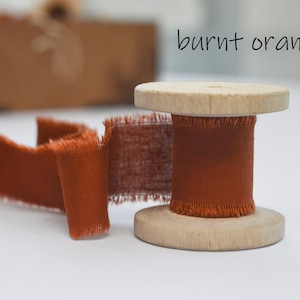 May include: A spool of burnt orange ribbon with frayed edges. The ribbon is wound around a wooden spool.