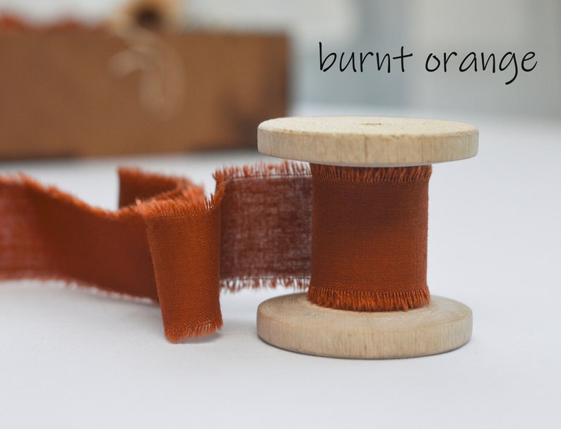 May include: A spool of burnt orange ribbon with frayed edges. The ribbon is wound around a wooden spool.