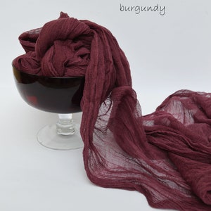 May include: Burgundy colored sheer fabric draped over a glass bowl. The fabric is soft and flowing, with a slightly wrinkled texture.