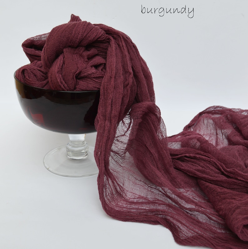 May include: Burgundy colored sheer fabric draped over a glass bowl. The fabric is soft and flowing, with a slightly wrinkled texture.