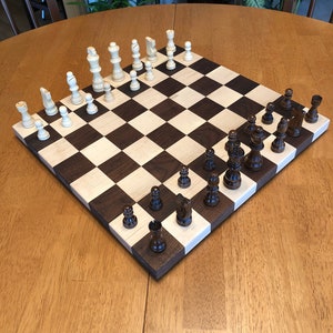 May include: A wooden chessboard with black and white squares. The board is set up with white and brown chess pieces. The board is on a wooden table.