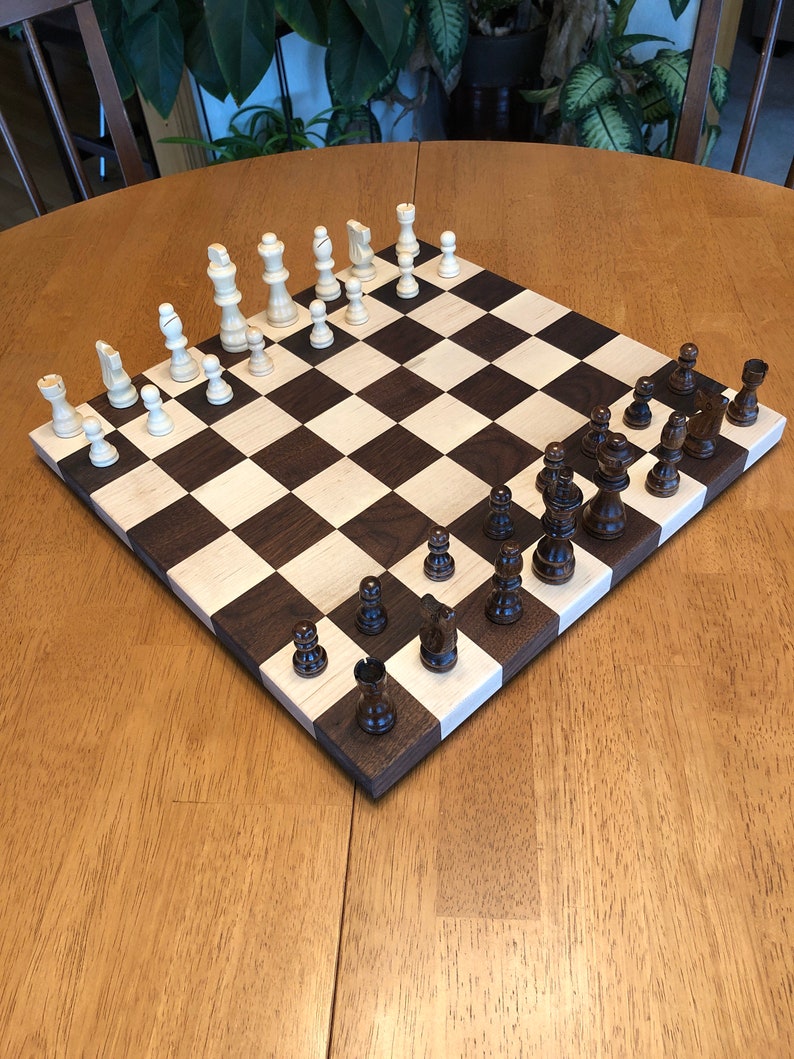 May include: A wooden chessboard with black and white squares. The board is set up with white and brown chess pieces. The board is on a wooden table.