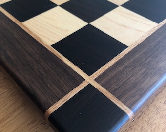 May include: Close-up of the corner of a wooden chessboard with a black and white checkered playing surface and a dark brown wood border.