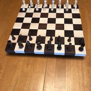 May include: A wooden chessboard with black and white squares. The chess pieces are arranged in their starting positions. The white pieces are made of light wood and the black pieces are made of dark wood.