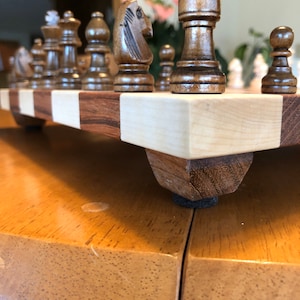 May include: A wooden chessboard with a set of chess pieces. The board is made of light and dark wood and has a checkered pattern. The pieces are made of dark wood and are in the starting position.