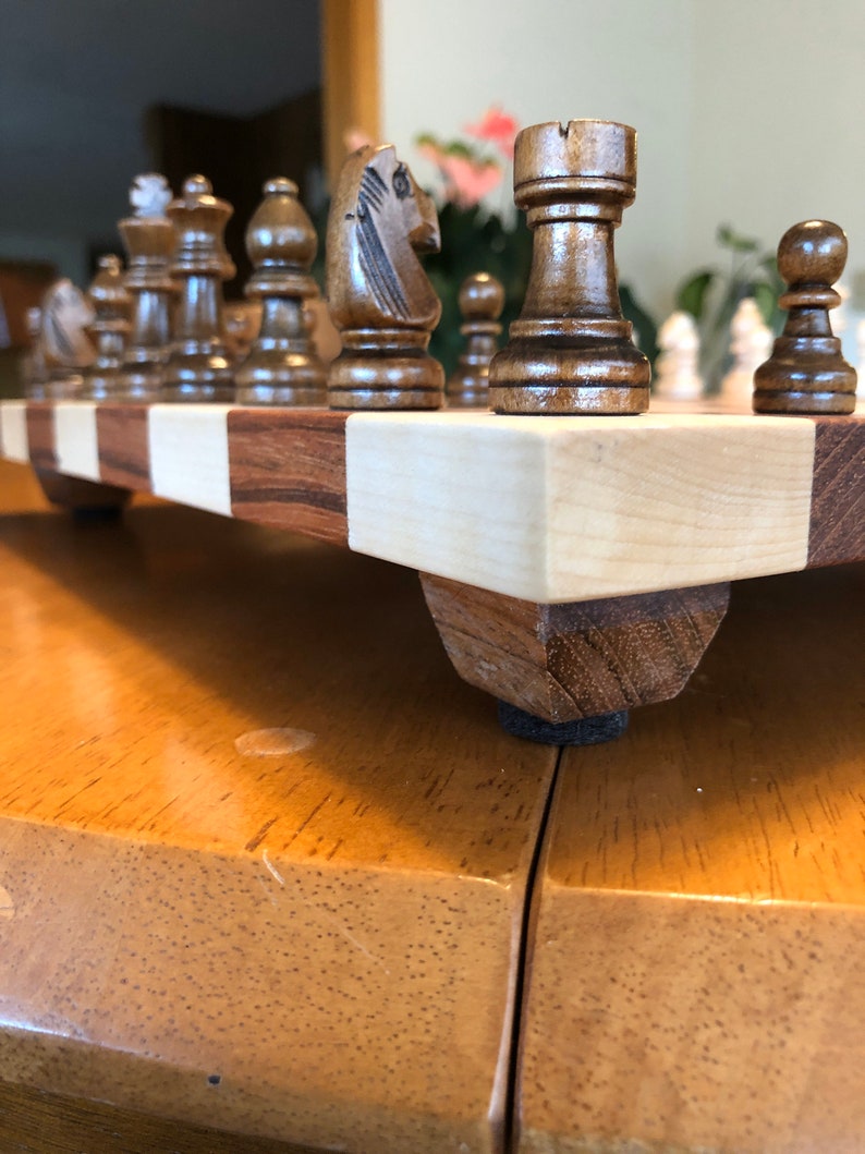 May include: A wooden chessboard with a set of chess pieces. The board is made of light and dark wood and has a checkered pattern. The pieces are made of dark wood and are in the starting position.