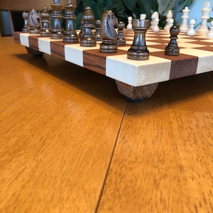 May include: A wooden chessboard with brown and white squares. The board has a set of chess pieces on it, including a knight, a bishop, a rook, and a pawn. The pieces are made of wood and have a dark brown finish.