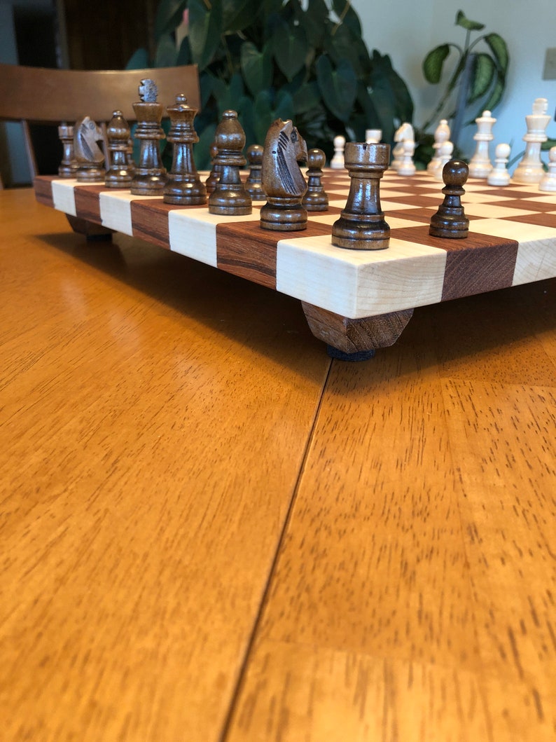 May include: A wooden chessboard with brown and white squares. The board has a set of chess pieces on it, including a knight, a bishop, a rook, and a pawn. The pieces are made of wood and have a dark brown finish.