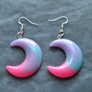 May include: A pair of crescent moon earrings with a pink and purple ombre effect and silver hooks.