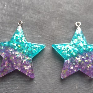 May include: Two turquoise and purple glitter star-shaped resin charms with silver jump rings.