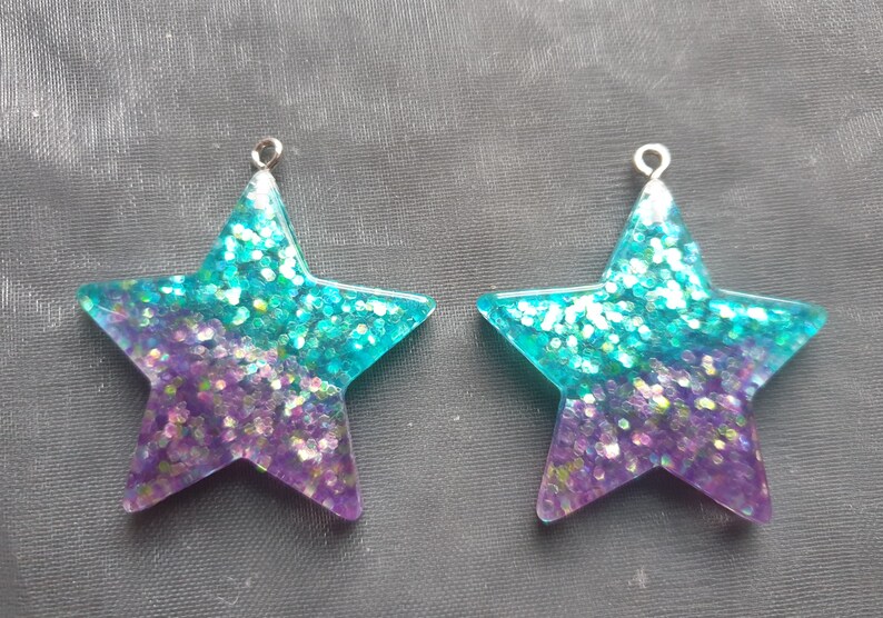 May include: Two turquoise and purple glitter star-shaped resin charms with silver jump rings.