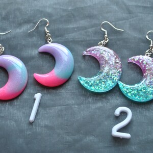 May include: A pair of crescent moon earrings with glitter embedded in the resin. The earrings are pink and blue with a gradient effect. The earrings are numbered 1 and 2.