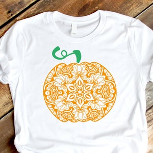 Puede incluir: Camiseta blanca con un diseño de calabaza mandala naranja y verde.