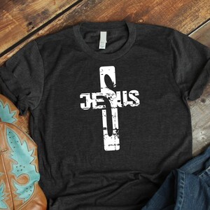 May include: A dark grey t-shirt with a white distressed cross and the word "JESUS" printed on it.