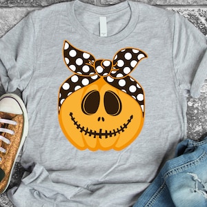 Puede incluir: Una camiseta gris con un gráfico de una calabaza naranja sonriente que lleva una bandana de lunares negros y blancos.