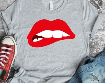 May include: A gray t-shirt with a red, open-mouthed lip design. The lip is biting its lower lip.
