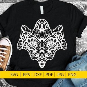 Puede incluir: Una camiseta negra con un diseño blanco, intrincado, en forma de fantasma. El diseño recuerda a una calavera de azúcar. El texto "SVG | EPS | DXF | PDF | JPG | PNG" está en la parte inferior de la imagen.