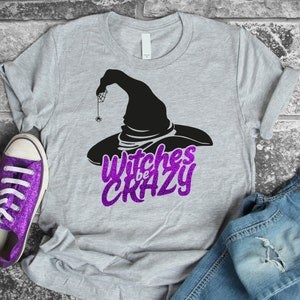 May include: A gray t-shirt with a black witch's hat and the text "Witches be Crazy" in purple glitter.