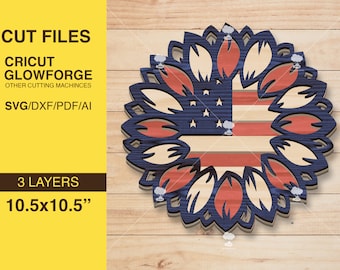 May include: A three-layer, 10.5 inch by 10.5 inch, layered design of a sunflower with an American flag in the center. The sunflower is made of red, white, and blue petals.