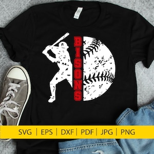 Puede incluir: Camiseta negra con una silueta blanca de un jugador de béisbol balanceando un bate. La palabra "BISON" está escrita verticalmente en rojo a la derecha del jugador. Una pelota de béisbol blanca con costuras rojas está detrás del jugador.