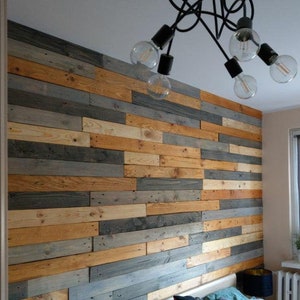 May include: A bedroom with a bed and a headboard made of reclaimed wood. The wall behind the bed is covered in a pallet wood wall. There is a black chandelier with five light bulbs hanging from the ceiling.
