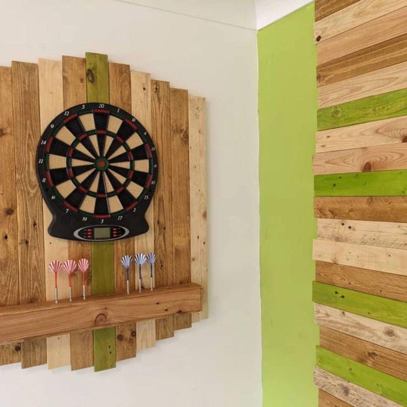 K&ouml;nnte beinhalten: Ein Dartboard mit einem Holzrahmen und einem Regal f&uuml;r Darts. Das Dartboard ist an einer Wand mit einem gr&uuml;nen und Holzpaneel-Hintergrund montiert.