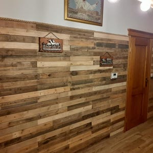 K&ouml;nnte beinhalten: Eine Wand, die mit wiederverwendeten Holzbrettern verkleidet ist, erzeugt einen rustikalen und modernen Look. Die Wand ist mit zwei Metallschilden dekoriert, eines mit einem Pferd und das andere mit einem geometrischen Muster.