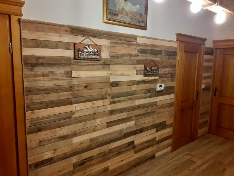 K&ouml;nnte beinhalten: Eine Wand, die mit wiederverwendeten Holzbrettern verkleidet ist, erzeugt einen rustikalen und modernen Look. Die Wand ist mit zwei Metallschilden dekoriert, eines mit einem Pferd und das andere mit einem geometrischen Muster.