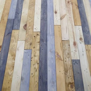 K&ouml;nnte beinhalten: Eine Wand aus wiederverwendeten Holzdielen in verschiedenen Graut&ouml;nen, Braun- und Beiget&ouml;nen. Die Dielen sind in einem versetzten Muster angeordnet, was einen rustikalen und einzigartigen Look erzeugt.