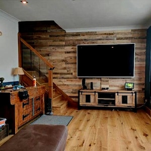 May include: A living room with a wooden wall, a large flat screen TV, and a wooden entertainment unit. The room has a wooden floor and a staircase leading up to the second floor.
