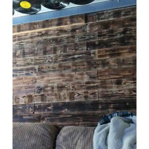 May include: A dark wood wall panelling with a rustic, reclaimed look. The wood has a natural, weathered finish with knots and grain patterns. The panelling is installed horizontally and creates a warm, inviting atmosphere.