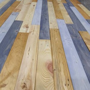 K&ouml;nnte beinhalten: Nahaufnahme einer Holzverkleidung aus wiederverwendeten Holzdielen. Die Dielen sind in Graut&ouml;nen, Hellbraun und Dunkelbraun gebeizt. Das Holz ist in einem zuf&auml;lligen Muster angeordnet, was einen rustikalen und einzigartigen Look erzeugt.