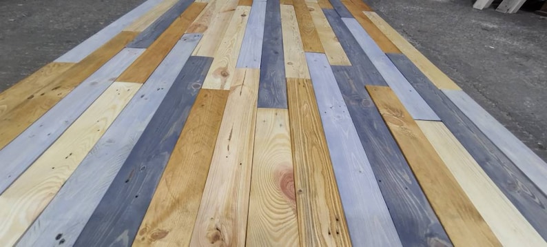 K&ouml;nnte beinhalten: Nahaufnahme einer Holzverkleidung aus wiederverwendeten Holzdielen. Die Dielen sind in Graut&ouml;nen, Hellbraun und Dunkelbraun gebeizt. Das Holz ist in einem zuf&auml;lligen Muster angeordnet, was einen rustikalen und einzigartigen Look erzeugt.