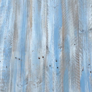 May include: A close-up of a weathered wood surface painted in a light blue colour. The wood planks are arranged vertically and have a rustic, distressed look.