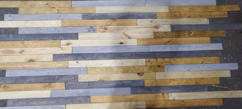K&ouml;nnte beinhalten: Eine Wand aus wiederverwendeten Holzdielen in verschiedenen Blaut&ouml;nen, Braun- und Beiget&ouml;nen. Die Dielen sind horizontal angeordnet und erzeugen einen rustikalen und modernen Look.