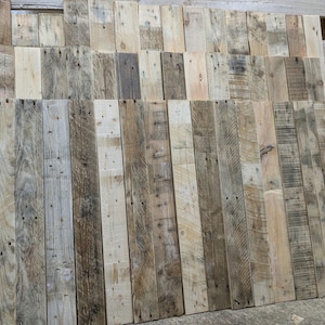 May include: A collection of reclaimed wood planks, featuring a variety of wood grains and colours, including light brown, dark brown, and grey. The planks are arranged in a vertical pattern, creating a rustic and natural look.