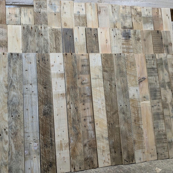 Op de afbeelding: Een verzameling gerecyclede houten planken, met verschillende houtnerven en kleuren, waaronder lichtbruin, donkerbruin en grijs. De planken zijn verticaal gerangschikt, wat een rustieke en natuurlijke uitstraling creëert.