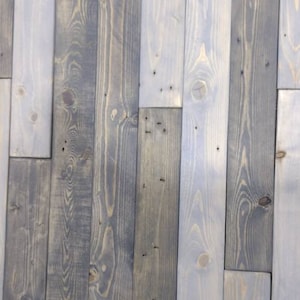 K&ouml;nnte beinhalten: Eine Wand aus wiederverwendeten Holzdielen, in Graut&ouml;nen und Wei&szlig; gestrichen. Das Holz hat ein rustikales, verwittertes Aussehen mit sichtbaren Knoten und Maserungen.