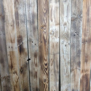 May include: A close-up of a weathered wooden wall made of reclaimed wood planks. The wood has a natural, rustic look with knots and grain patterns. The planks are arranged vertically and have a light brown colour with darker brown streaks.