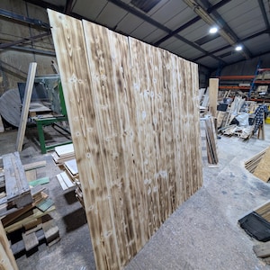 May include: A large panel of reclaimed wood planks with a rustic, weathered look. The wood has a natural, light brown colour with dark brown streaks and knots. The planks are arranged vertically and have a rough, textured surface.